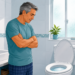 Ilustración de un hombre mayor en pijama parado en un baño luminoso, mirando pensativo hacia el inodoro.