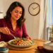 Mujer adulta come un plato con pollo, cereales y verduras junto a un reloj de pared en un comedor iluminado por el sol.