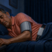 Hombre duerme de lado con un manguito de presión arterial conectado a un monitor portátil durante la noche.