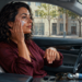 Mujer sentada en el interior de un automóvil aplica crema en el rostro mientras recibe luz solar a través de la ventanilla.