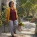 Mujer mayor sube unas escaleras al aire libre mientras lleva una bolsa de tela con alimentos en un entorno arbolado.