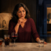 Mujer en una cocina de noche observa varias bebidas sobre la encimera, con un vaso de agua, café, té, refresco y vino, mientras al fondo se ve un baño iluminado.