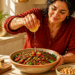 Mujer exprime medio limón sobre un plato de lentejas con verduras y hojas verdes en una cocina iluminada por el sol.
