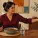 Mujer sentada a la mesa aparta una taza de bebida caliente mientras tiene delante un plato de legumbres y un vaso de agua.