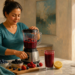 Mujer en una cocina prepara una bebida de frutos rojos en una batidora, con fresas, arándanos, moras, frambuesas, un vaso de la bebida y unas zapatillas junto a una puerta abierta.