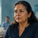 Mujer adulta con sudor visible en la frente y el rostro, sentada en una sala junto a un vaso de agua y una caja de pañuelos.