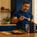 Hombre atlético añade una medida de proteína en polvo a un vaso mezclador, junto a un plato con salmón, legumbres y verduras y un tensiómetro sobre la mesa.