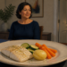 Mujer de mediana edad sentada a la mesa frente a un plato con pescado, patata cocida, calabacín y zanahoria durante la cena.