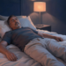 Un hombre adulto con los ojos cerrados acostado boca arriba en una cama, buscando conciliar el sueño en un dormitorio con iluminación tenue.