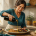 Mujer adulta vierte aceite de oliva desde una botella sobre un plato con pescado, garbanzos y verduras en una cocina luminosa.