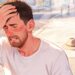 Un hombre afectado por el calor extremo se sujeta la frente con expresión de malestar mientras suda copiosamente en una calle soleada, ilustrando los síntomas de un golpe de calor.