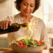 Una mujer vierte aceite de oliva virgen extra desde una botella de vidrio oscuro sobre una ensalada fresca en una cocina luminosa y de estilo rústico.