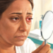 Mujer observando de cerca su ojo enrojecido y con lágrimas en un espejo de mano dentro del baño para evaluar síntomas de conjuntivitis o irritación ocular.