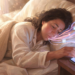 Mujer recostada en la cama por la mañana extendiendo la mano hacia su teléfono móvil en la mesita de noche mientras brotan destellos y ondas de la pantalla.