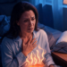 Mujer sentada en la cama por la noche con una mano en el pecho y gesto de dolor, mostrando los efectos del reflujo gastroesofágico nocturno.