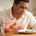 Hombre con expresión de malestar sosteniendo su mano sobre el estómago frente a un plato de comida, representando el dolor abdominal y los síntomas de la gastritis.