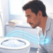 Un hombre en pijama observa con preocupación el interior de un inodoro lleno de una densa capa de espuma blanca y azulada dentro de un baño iluminado.