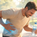 Hombre sufriendo un cólico nefrítico (dolor renal) agudo en el costado, sosteniendo una botella de agua, en un parque soleado y caluroso, con ondas de dolor ilustradas.