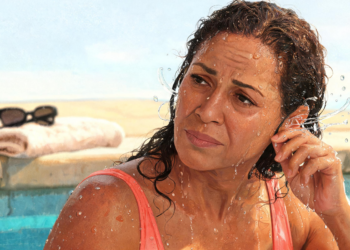 Mujer con el cabello mojado dentro de una piscina tocándose la oreja con expresión de molestia, representando la sensación de oído tapado en verano.