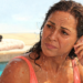 Mujer con el cabello mojado dentro de una piscina tocándose la oreja con expresión de molestia, representando la sensación de oído tapado en verano.