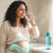 Una mujer sonriente bebe un vaso de agua en un ambiente iluminado, mientras un gráfico brillante de ondas azules resalta su zona abdominal.