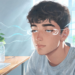 Un joven mira hacia el horizonte junto a una ventana para descansar la vista tras usar su ordenador, representando la prevención del ojo seco digital.
