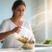 Una mujer vierte una ensalada desde un táper de plástico a un tazón de vidrio en una cocina luminosa, ilustrando la liberación de partículas de microplásticos en los alimentos.