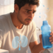 Un hombre sudoroso con expresión preocupada sostiene una botella de agua en un baño, mostrando una ilustración gráfica de los riñones en su torso para representar problemas de micción y función renal.