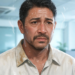 Un hombre de mediana edad en una oficina con el rostro cubierto de gotas de sudor y la camisa empapada, mostrando una expresión de malestar debido a la sudoración excesiva.