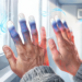 Primer plano de dos manos cuyas puntas de los dedos se tornan blancas y azules debido al frío, ilustrando los síntomas característicos del fenómeno de Raynaud junto a una ventana con condensación y bajo el flujo de un aire acondicionado.