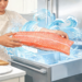 Persona cocinando colocando un filete de salmón fresco en el congelador, rodeado de efectos visuales de hielo.