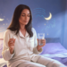 Mujer en pijama tomando un suplemento de melatonina con un vaso de agua antes de dormir, concepto de rutina nocturna saludable.