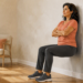 Mujer adulta realizando una sentadilla isométrica contra la pared, con las rodillas flexionadas y los pies apoyados en el suelo de una habitación luminosa.