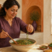 Mujer adulta preparando una ensalada con verduras de hoja verde, legumbres y semillas en una cocina iluminada por luz natural.