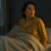 Mujer sentada en la cama durante la madrugada, con expresión de alerta, en un dormitorio tenue y junto a un reloj sobre la mesita de noche, en una escena relacionada con el despertar nocturno.