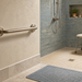 Baño adaptado con barra de apoyo en la pared, ducha a ras de suelo, taburete de baño y alfombra antideslizante para prevenir caídas en casa.