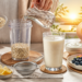 Preparación de agua de avena en una cocina, con copos de avena en una batidora mientras se vierte agua, acompañados de un vaso con la bebida, frutas, yogur, huevo, limón y canela.
