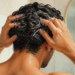 Hombre en la ducha masajea el cuero cabelludo con champú mientras se lava el pelo, con espuma visible y un espejo al fondo.