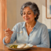 Mujer mayor sentada a la mesa comiendo una comida suave con arroz, verduras y un filete blanco, acompañada de un vaso de agua.