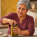 Mujer mayor de cabello gris abriendo un frasco de vidrio con ambas manos en una cocina, en una escena relacionada con la fuerza y destreza de las manos después de los 60.