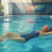 Mujer mayor con traje de baño azul flotando relajadamente boca arriba en una piscina cubierta, con las piernas extendidas y los brazos abiertos sobre el agua.