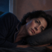 Mujer despierta acostada de lado con la cabeza apoyada sobre la almohada durante la noche, junto a un vaso de agua sobre la mesita.