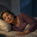 Mujer mayor acostada de lado en la cama durante la noche, con expresión de mareo o desorientación mientras mira hacia un lado.