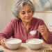 Mujer mayor sentada a una mesa comparando dos boles de yogur blanco mientras sostiene una cucharada, acompañada de frutos rojos, arándanos y nueces.