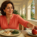 Mujer de mediana edad sentada a la mesa durante una comida, con pescado, legumbres y verduras en el plato, mientras toma una manzana roja con la mano.