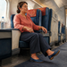Mujer adulta sentada en un asiento de transporte durante un viaje, con una botella de agua a su lado y una pierna extendida hacia delante.