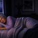 Mujer mayor durmiendo de lado en una cama durante la noche, arropada con mantas y apoyada sobre una almohada en una habitación oscura y tranquila.