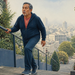 Hombre mayor subiendo unas escaleras al aire libre mientras se apoya en la barandilla, con expresión de esfuerzo y una ciudad desenfocada al fondo.
