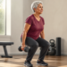 Mujer mayor realizando una sentadilla con dos mancuernas en un gimnasio, en una escena relacionada con el entrenamiento de fuerza para fortalecer los huesos después de los 60.