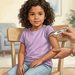 Niña pequeña sentada en una silla mientras un adulto le coloca un termómetro digital bajo el brazo en una habitación luminosa de casa.